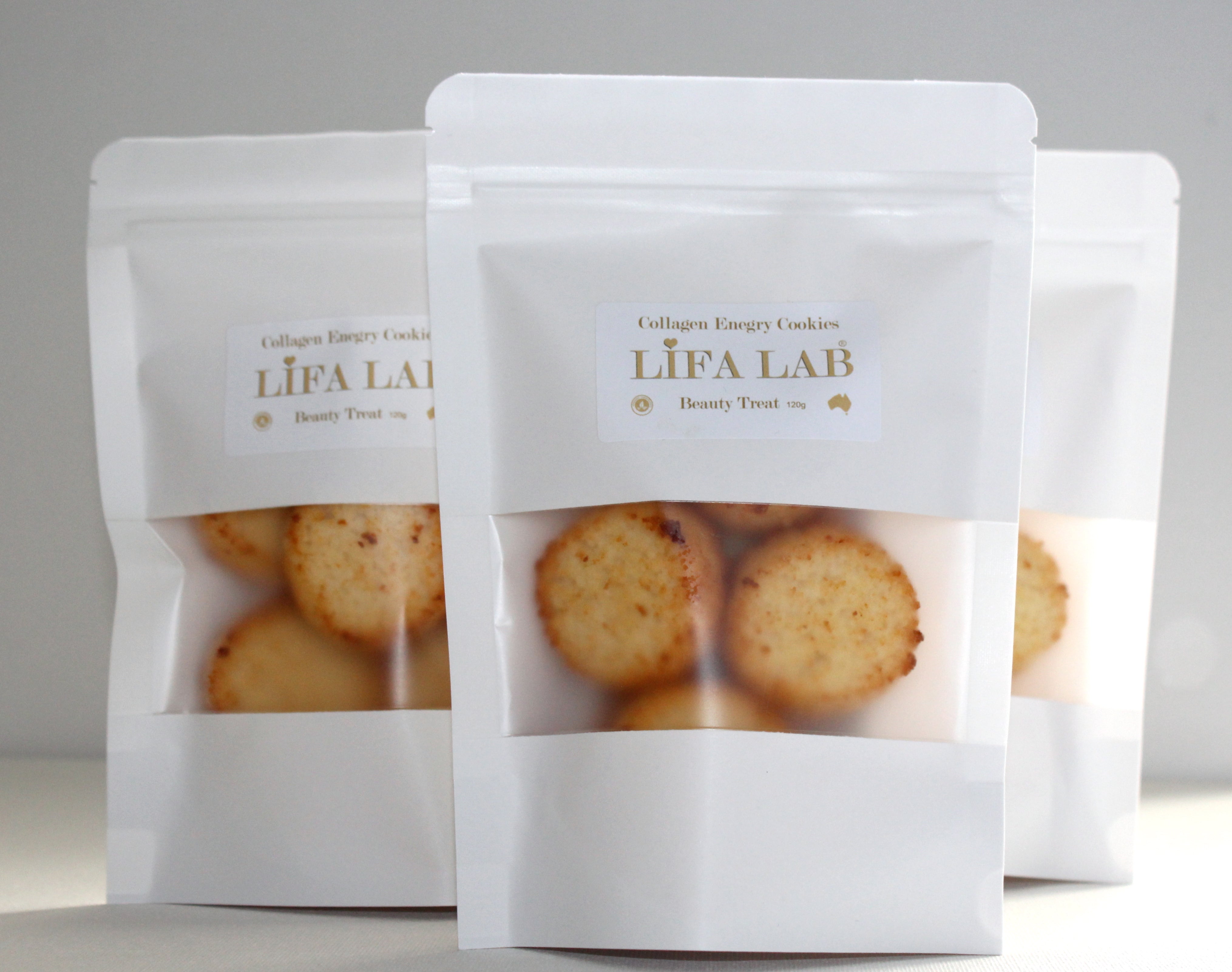 three white packs of collagen and energy cookies standing on a white table with white background with lifa lab logo 